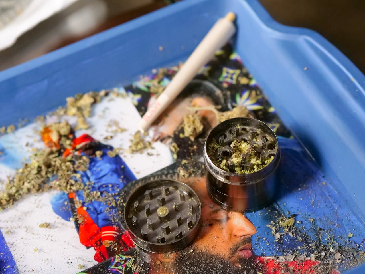 Cannabis grinder filled with marijuana next to a rolled joint on a colorful tray. Perfect for cannabis culture imagery.
