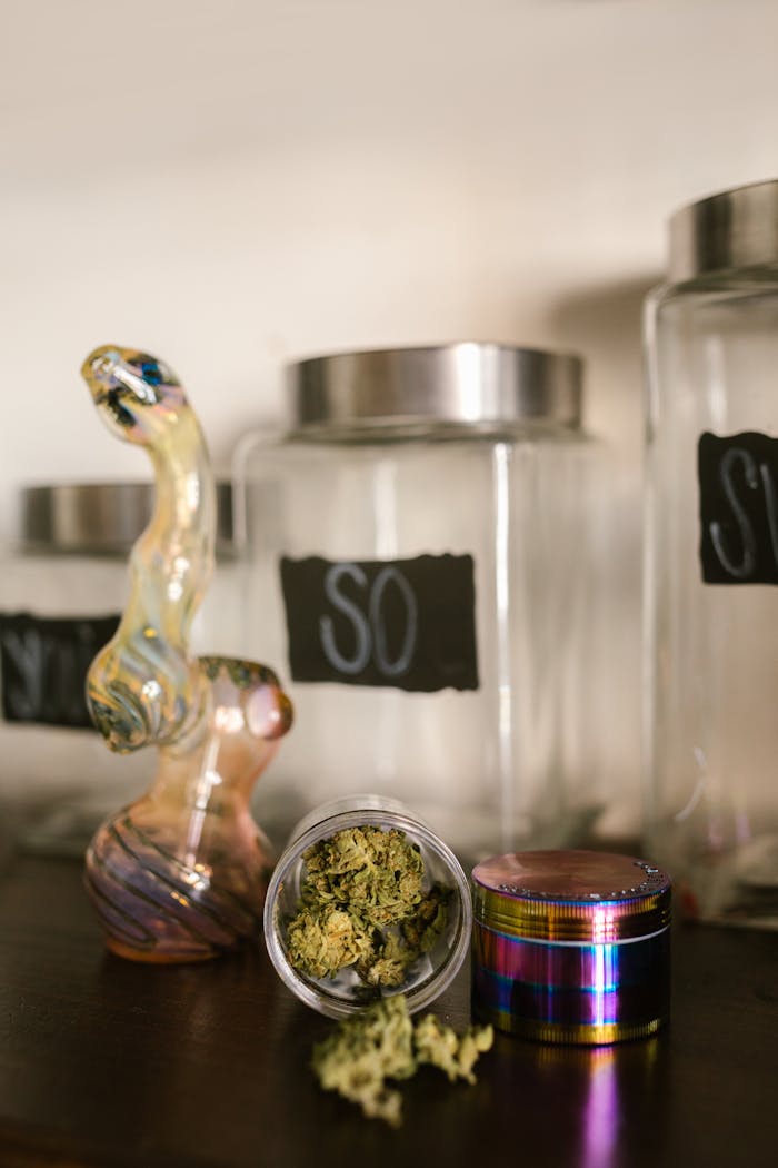Close-up of cannabis, a glass pipe, and a colorful grinder on a shelf.
