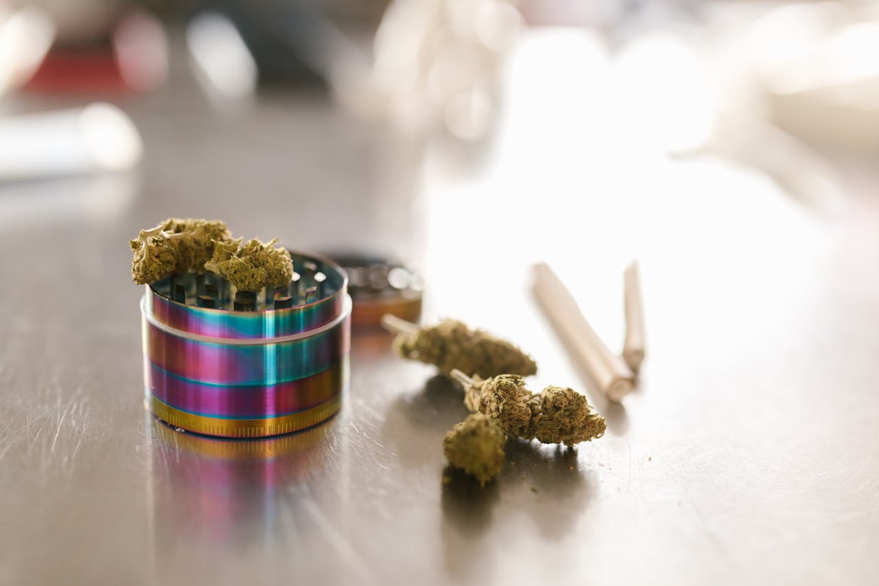 Cannabis buds with a colorful grinder on a reflective surface in natural light.
